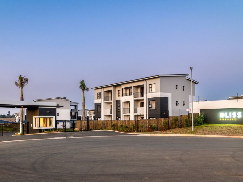 Modern apartment complex entrance featuring a secure gatehouse, paved driveway, and contemporary building architecture with private balconies.