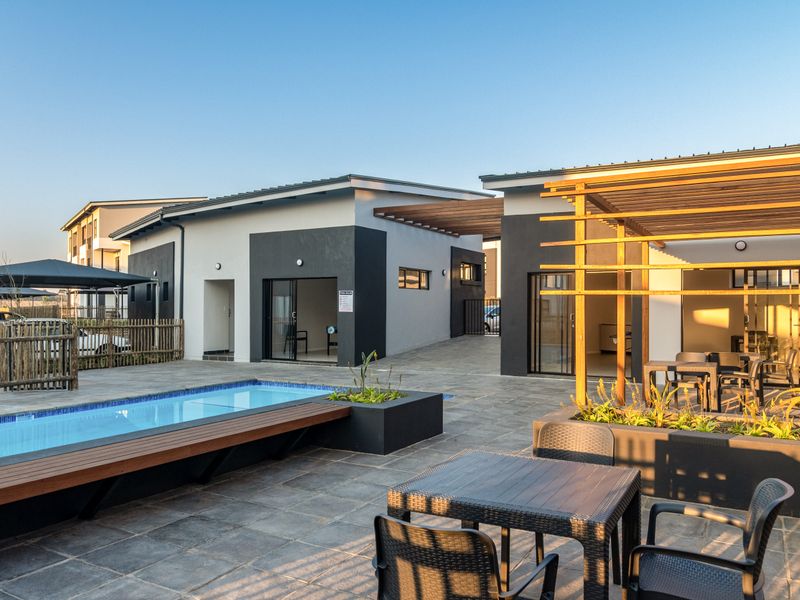 Modern outdoor entertainment area featuring a swimming pool, timber pergola, and tiled patio space with built-in planters and direct access to the apartment units.