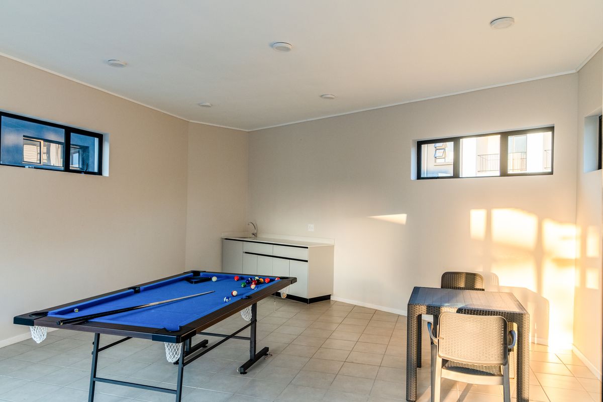 A spacious living area featuring tiled flooring, recessed lighting, and a convenient built-in kitchenette cabinet with a sink.