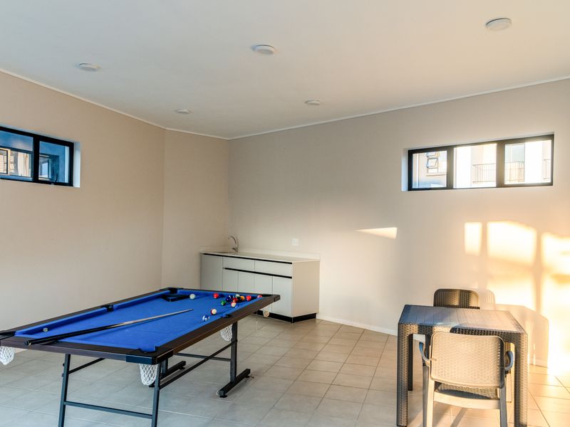 A spacious living area featuring tiled flooring, recessed lighting, and a convenient built-in kitchenette cabinet with a sink.