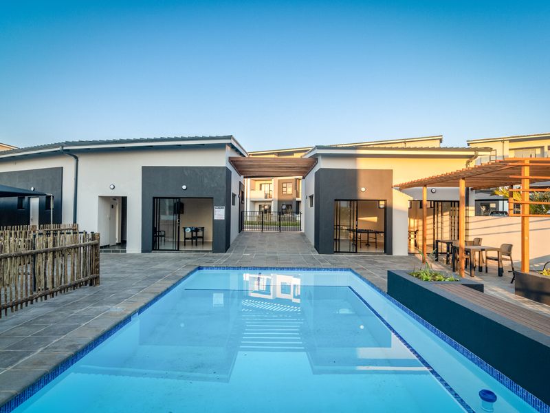 A well-maintained communal pool area featuring a tiled deck, timber pergola, and modern building architecture with sliding glass access points.