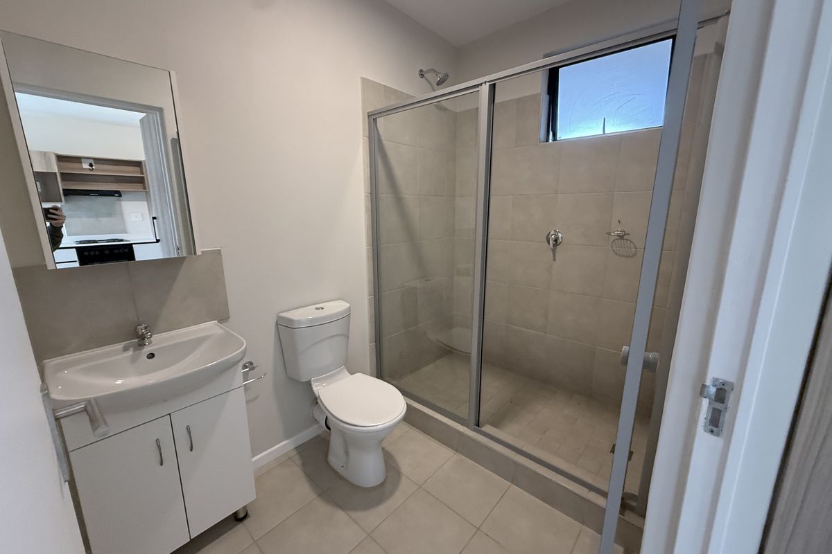 A clean, modern bathroom featuring a walk-in shower with glass enclosure, a vanity cabinet with basin, and neutral floor tiling.