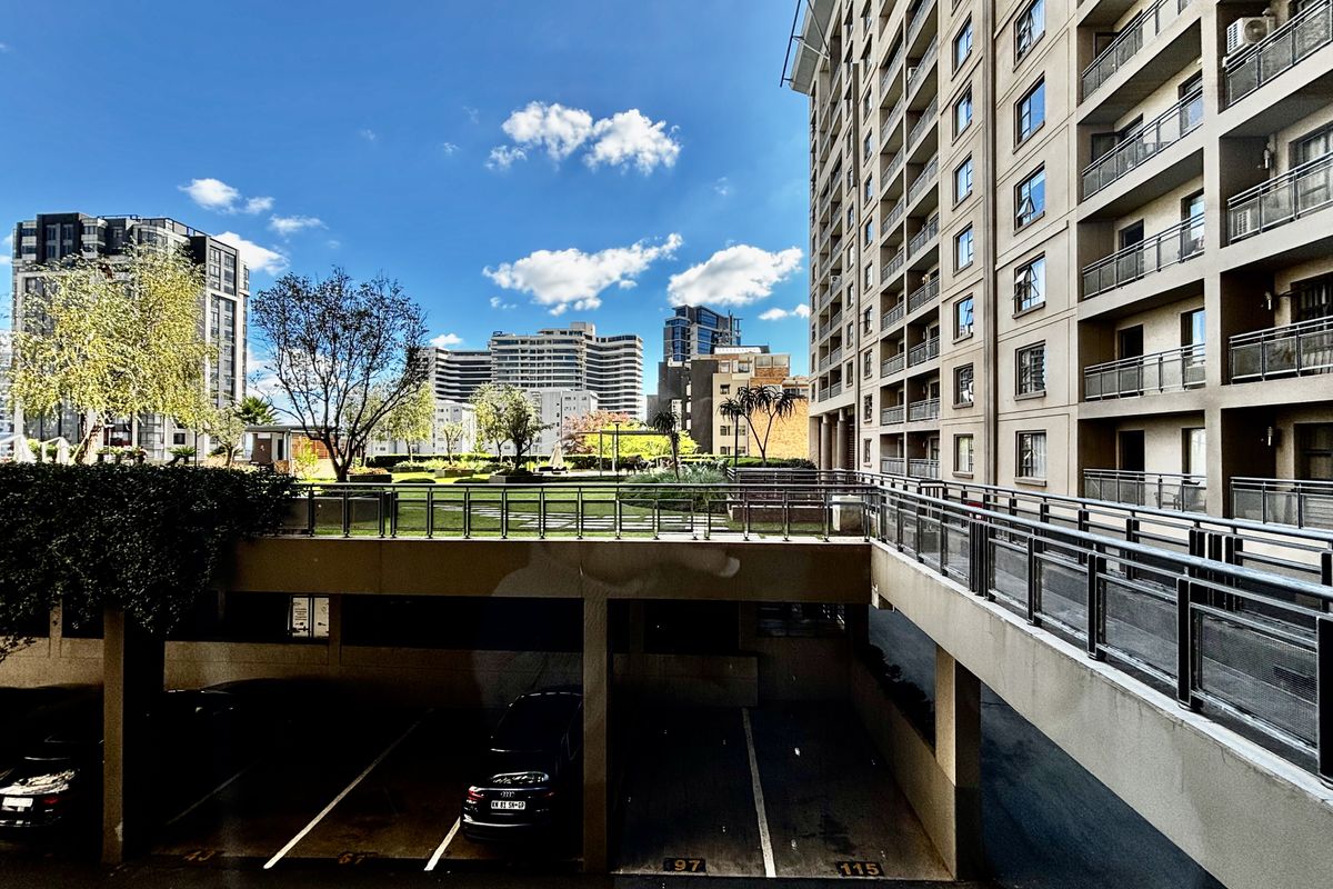 View of the apartment complex exterior featuring undercover parking bays, an elevated garden terrace, and modern multi-story building architecture.