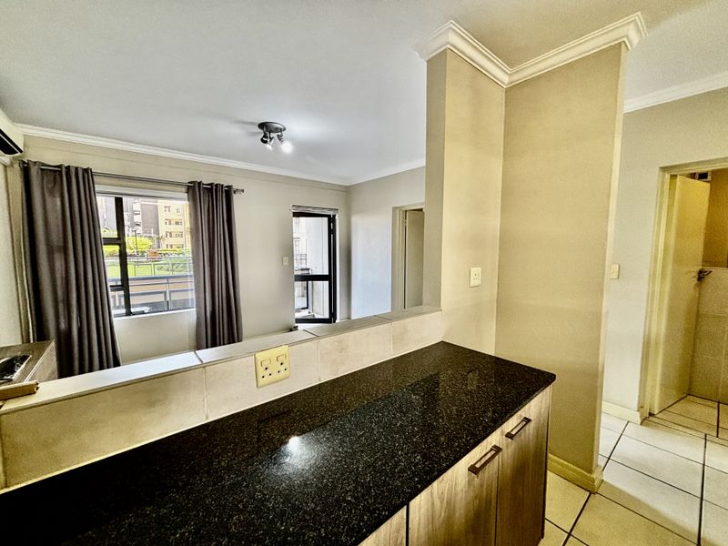 Open plan living area featuring a kitchen breakfast bar with granite countertops, tiled flooring, and access to a balcony.