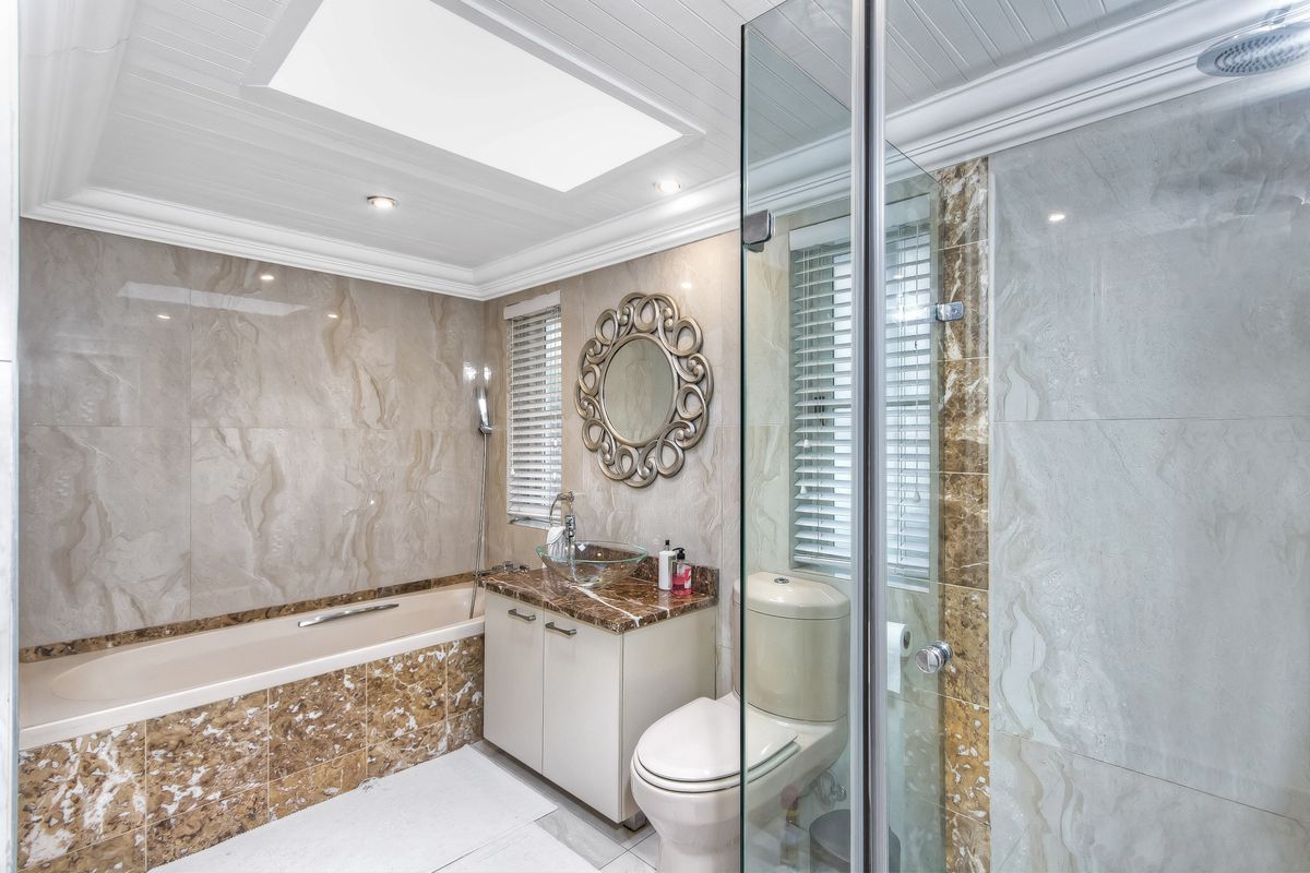 Modern bathroom featuring a built-in bathtub, glass-enclosed shower, marble-topped vanity, and a skylight providing natural light.