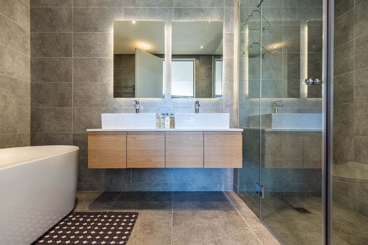 Modern bathroom featuring a floating double vanity with vessel sinks, a freestanding bathtub, and a glass-enclosed walk-in shower with grey tiled walls.