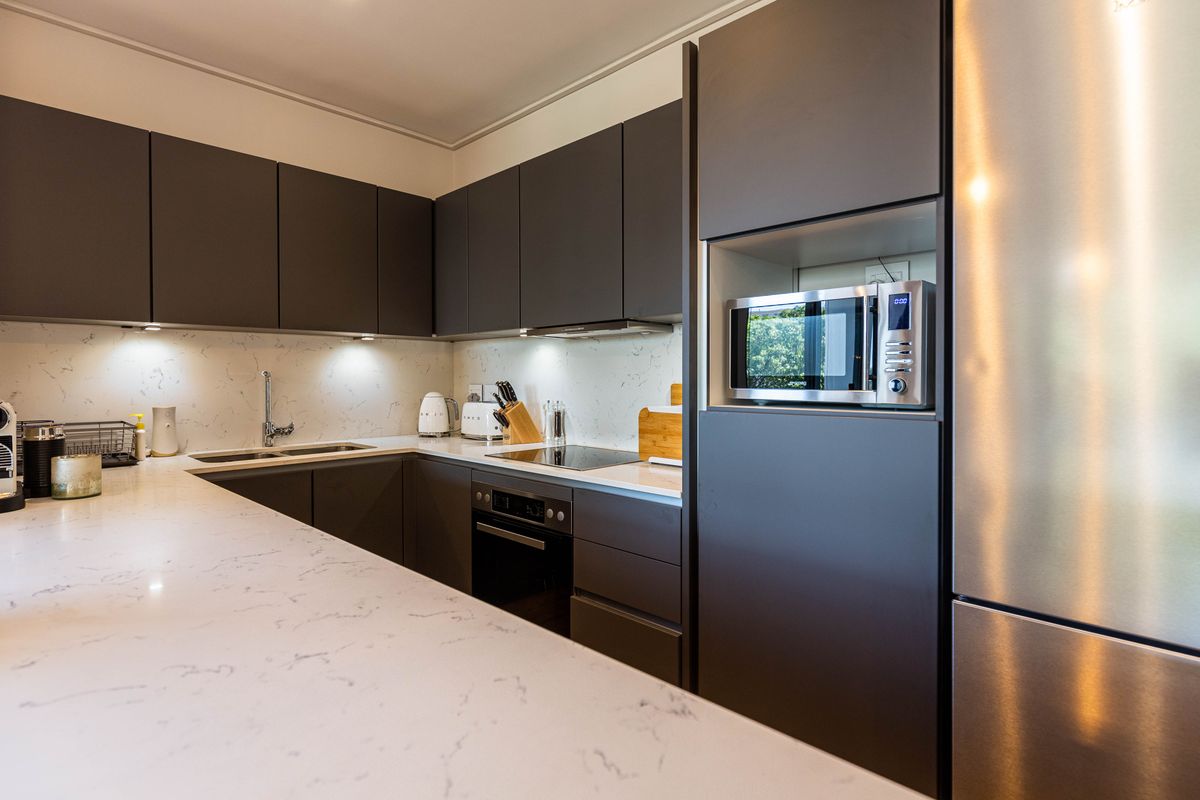 Modern kitchen featuring dark cabinetry, stone countertops, integrated oven, induction hob, and built-in microwave, offering a sleek and functional culinary space.