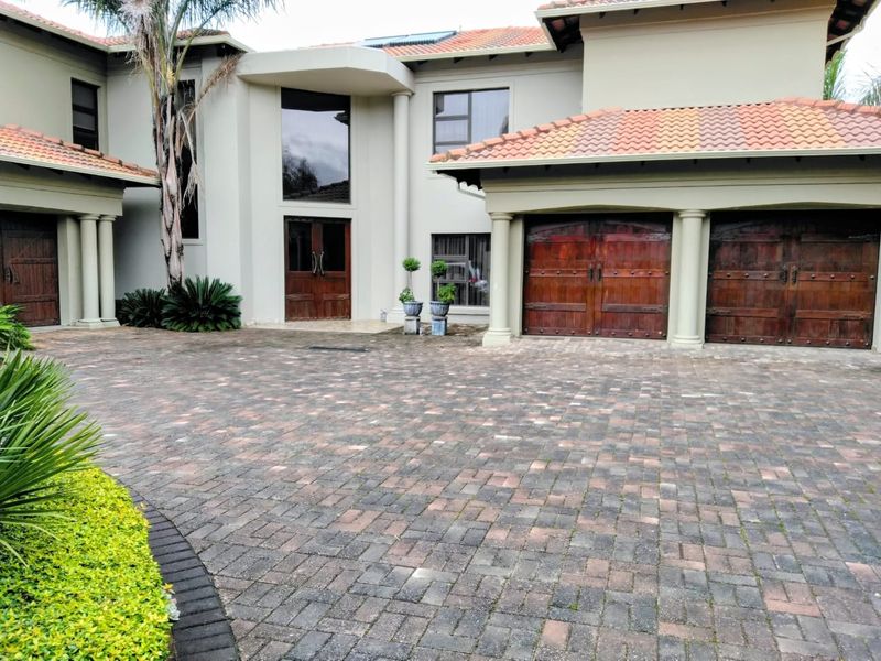 Front elevation of a double-story residence featuring a paved driveway, double wooden garage doors, and a prominent entrance with architectural columns.