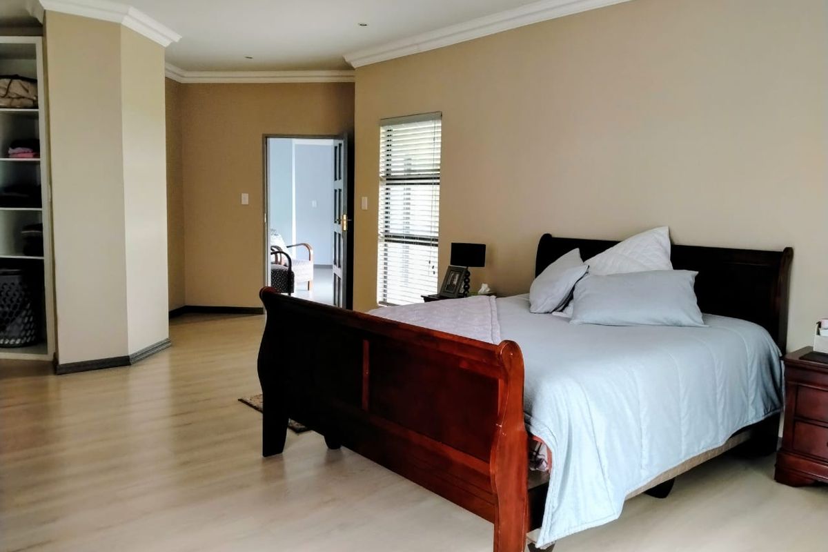 Spacious bedroom featuring light-toned laminate flooring, built-in shelving unit, and large windows with fitted blinds, offering a neutral and functional living space.