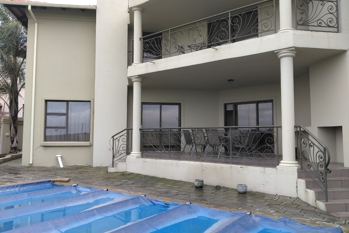 Rear view of a multi-story house featuring a covered patio, balcony with decorative wrought iron railings, and a swimming pool with a cover.