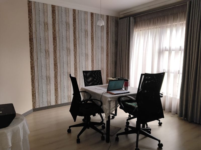 A functional office space featuring wood-look laminate flooring, a decorative vertical-plank feature wall, and floor-to-ceiling curtains.