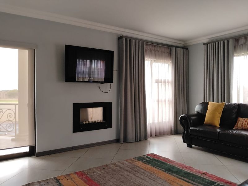 A well-maintained living room featuring a built-in fireplace, tiled flooring, and large windows with floor-to-ceiling curtains providing ample natural light.