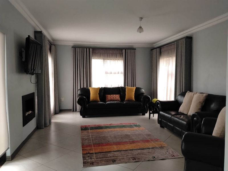 A spacious living room featuring tiled flooring, a built-in fireplace, and large windows with floor-to-ceiling curtains.
