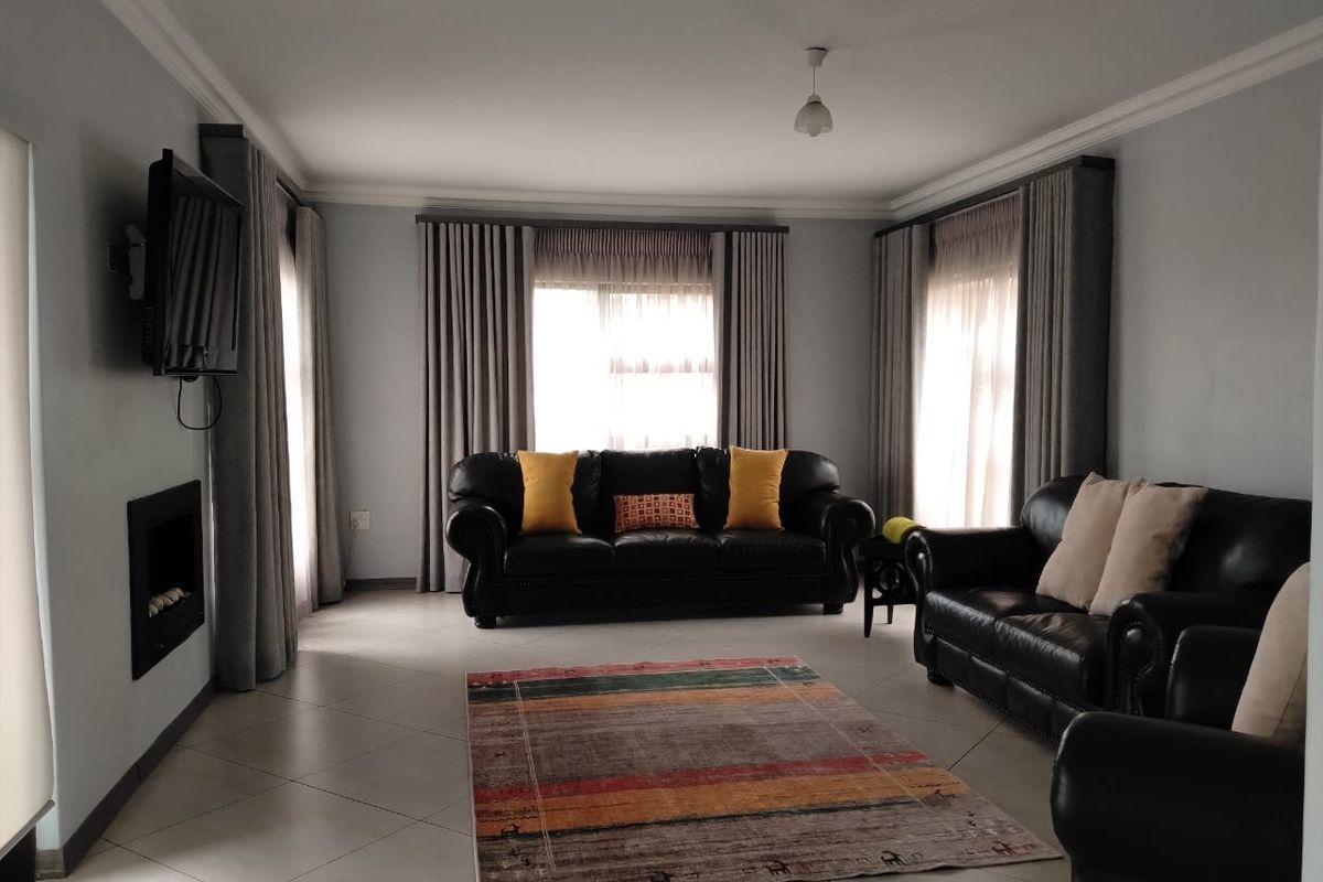 A spacious living room featuring tiled flooring, a built-in fireplace, and large windows with floor-to-ceiling curtains.