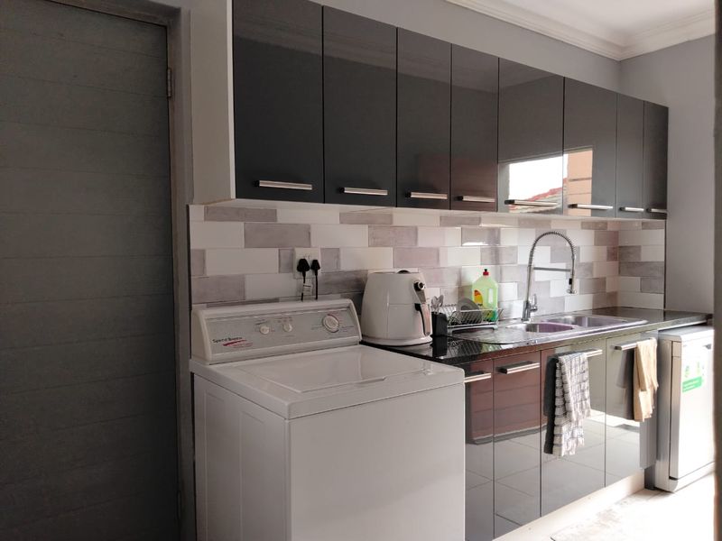 A functional laundry area featuring modern high-gloss cabinetry, a tiled backsplash, and a stainless steel sink with a gooseneck faucet.