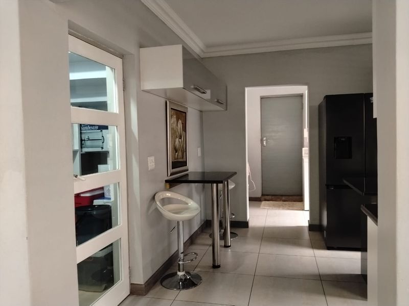 A modern kitchen area featuring tiled flooring, built-in cabinetry, and a breakfast bar, leading through to a secondary utility or laundry space.