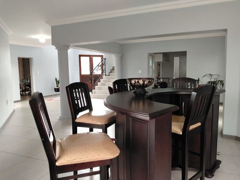 Open plan living area featuring a built-in bar, tiled flooring, decorative columns, and a staircase leading to the upper level.