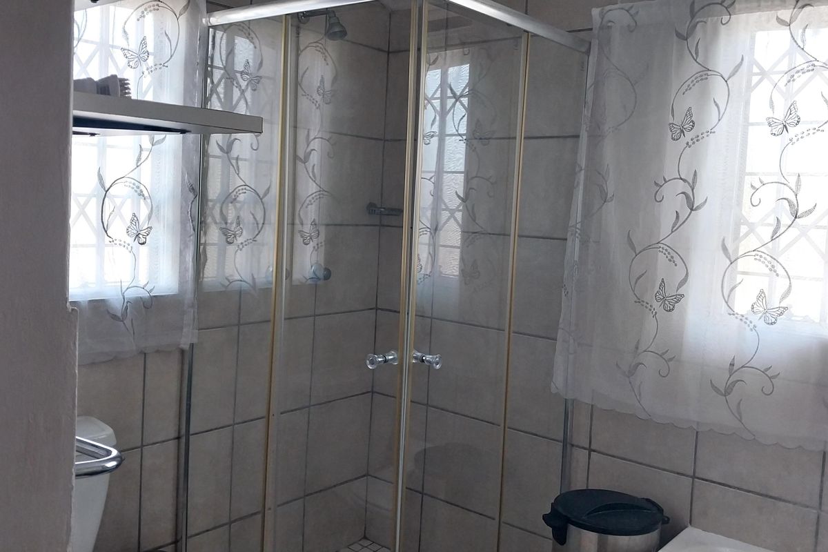 A functional bathroom featuring a glass shower enclosure, tiled walls, and security bars on the windows.