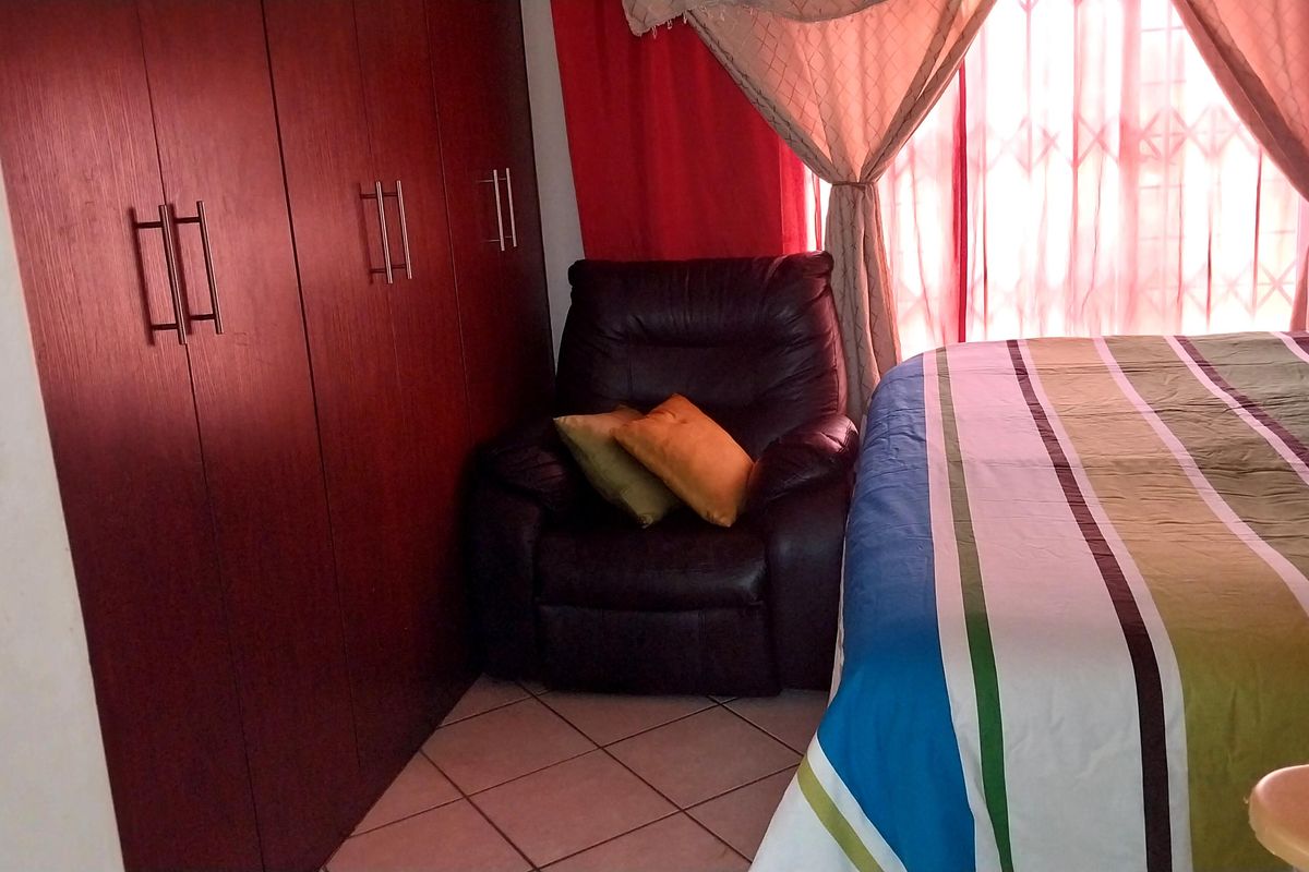 A bedroom featuring built-in wooden cupboards and tiled flooring, with a security gate installed at the window.