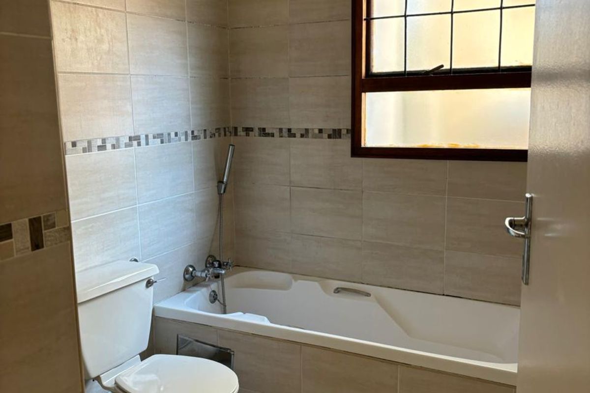 A functional bathroom featuring neutral wall and floor tiling, a built-in bathtub with a handheld shower attachment, and a standard toilet.