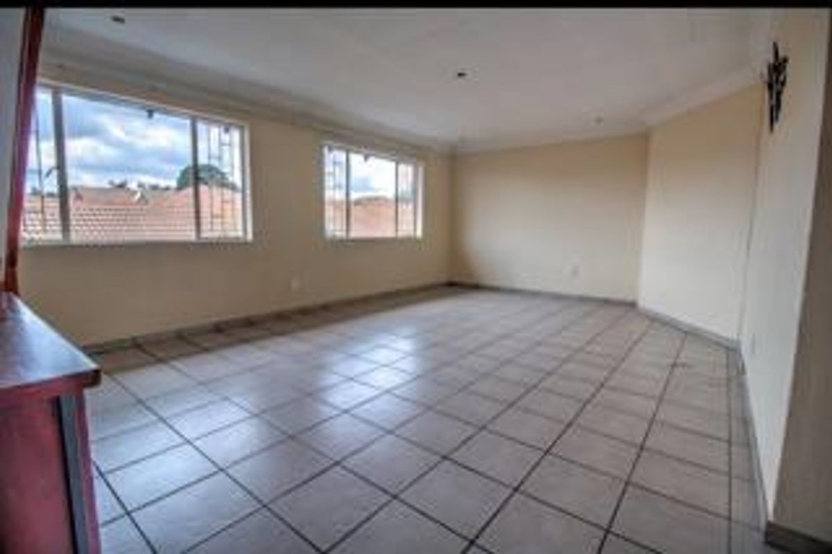 A spacious, empty living area featuring neutral tiled flooring, large windows providing natural light, and recessed ceiling lighting.
