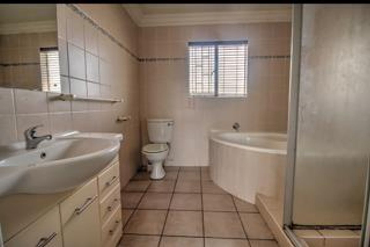 A functional bathroom featuring a corner bathtub, separate shower, vanity basin, and toilet with neutral wall and floor tiling.