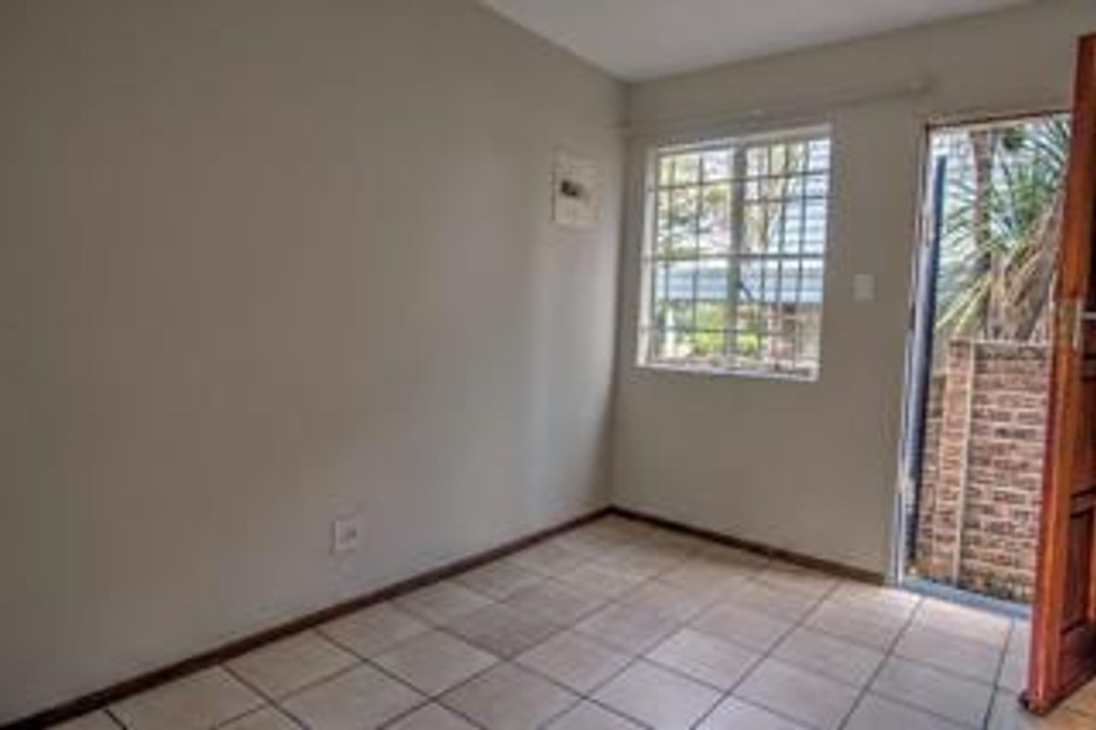 A vacant bedroom featuring neutral walls, tiled flooring, and a secure window with exterior access via a timber door.