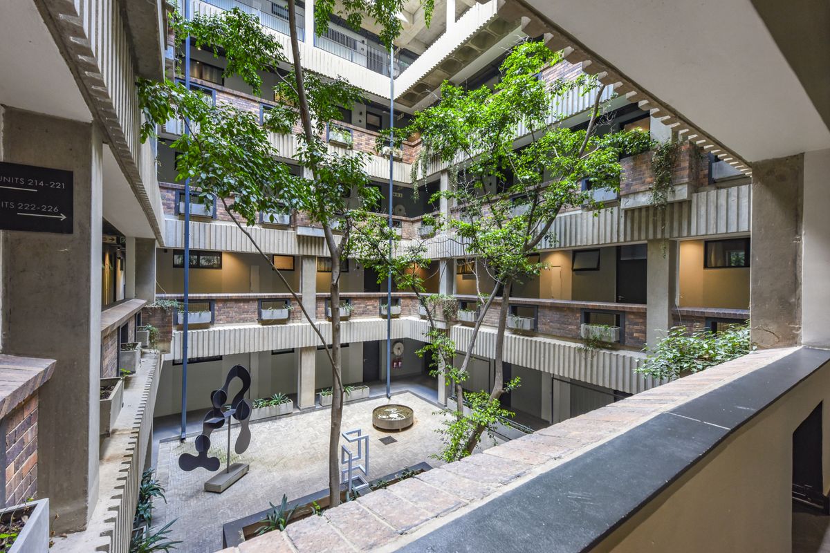 A view of the apartment complex's central open-air atrium, featuring multi-level walkways, brick and concrete architecture, and a landscaped courtyard with mature trees.