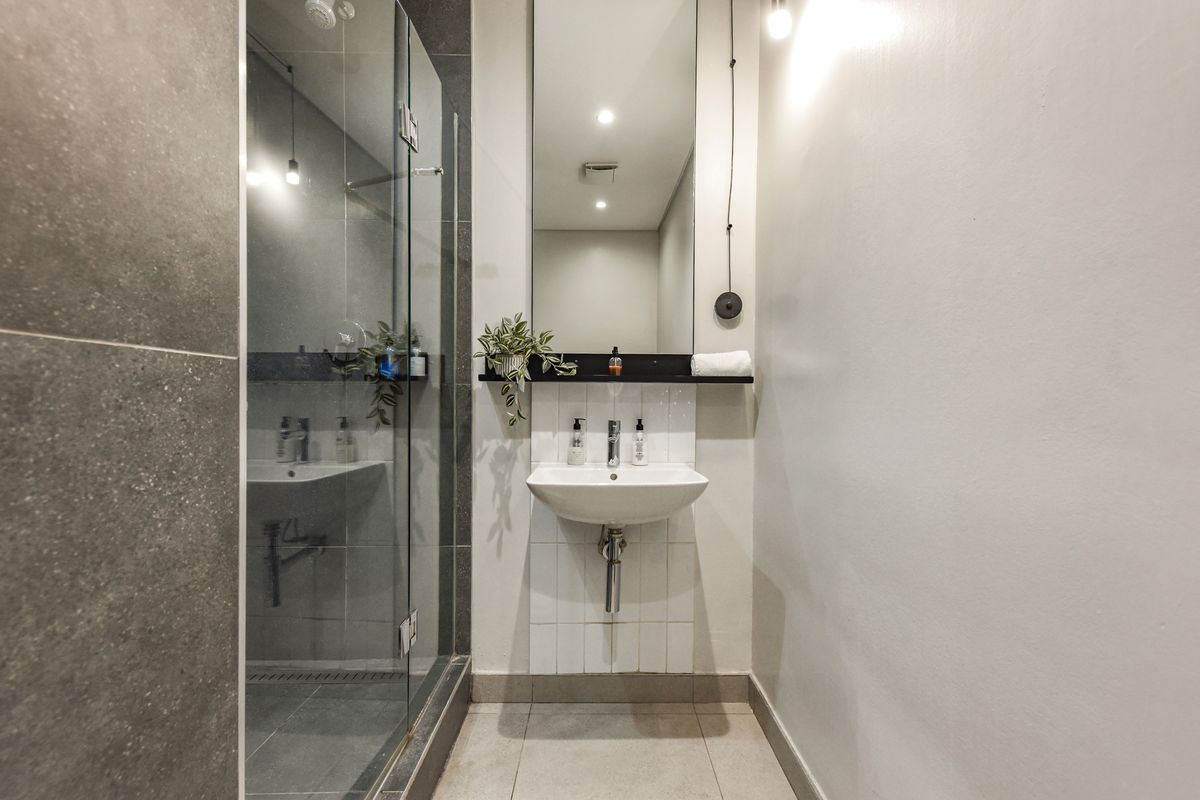 Modern bathroom featuring a glass-enclosed shower with dark grey tiling, a wall-mounted basin, and a large vanity mirror.
