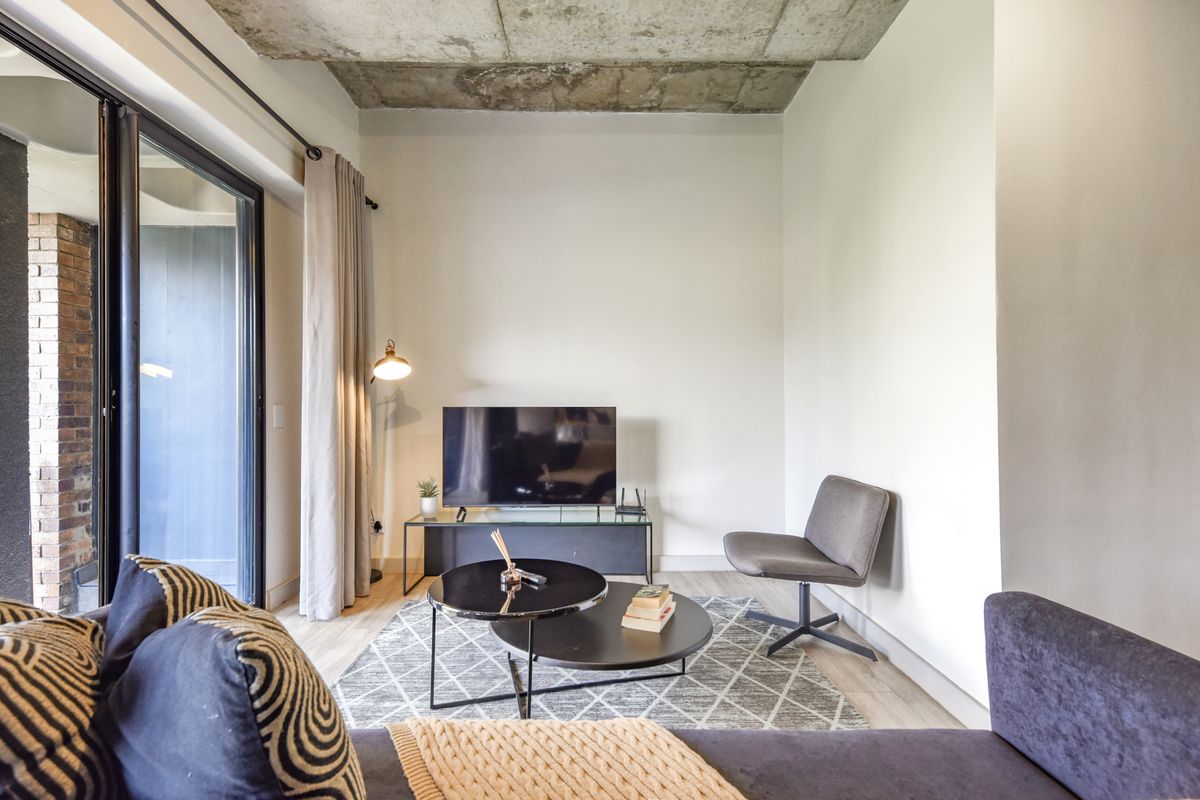 Modern living area featuring an exposed concrete ceiling, light wood-look flooring, and large sliding glass doors leading to an outdoor balcony.