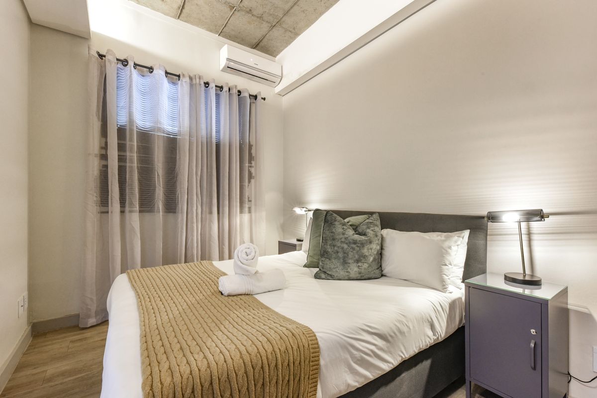 A modern bedroom featuring an exposed concrete ceiling, wood-look flooring, and a wall-mounted air conditioning unit.
