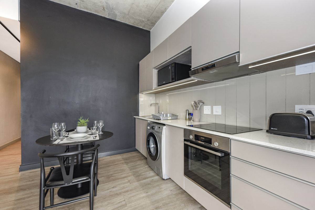 Modern kitchen featuring sleek cabinetry, integrated oven, hob, extractor fan, and built-in laundry appliance, set against a striking dark feature wall.