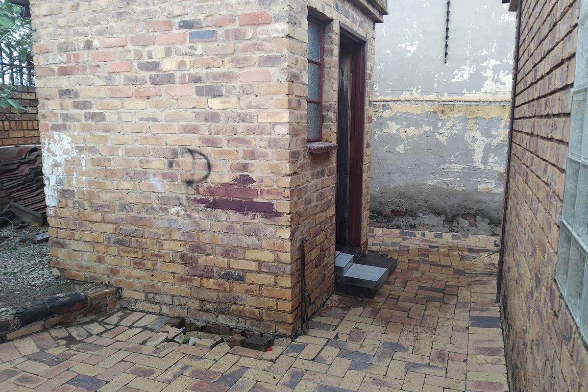 Exterior view of a small brick utility structure with paved surround, showing signs of significant wear and maintenance requirements.