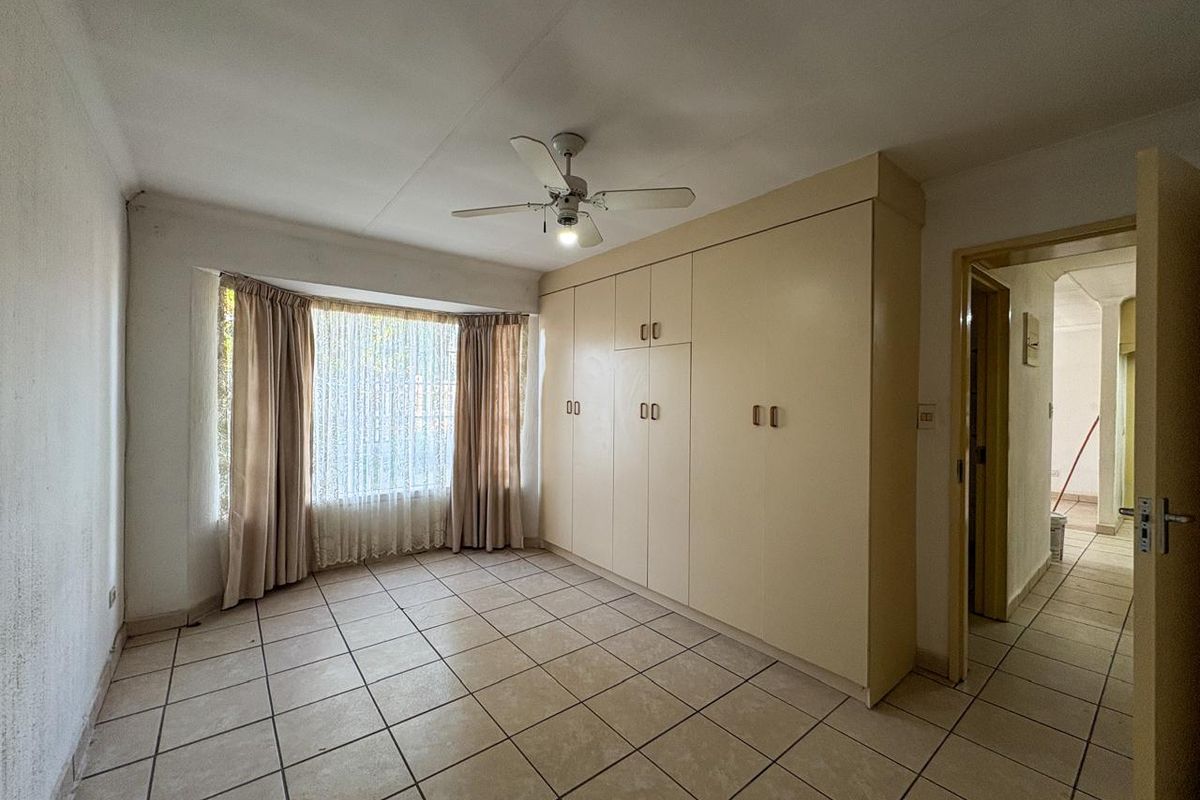 A bedroom featuring built-in cupboards, tiled flooring, and a ceiling fan, with a large window providing natural light.