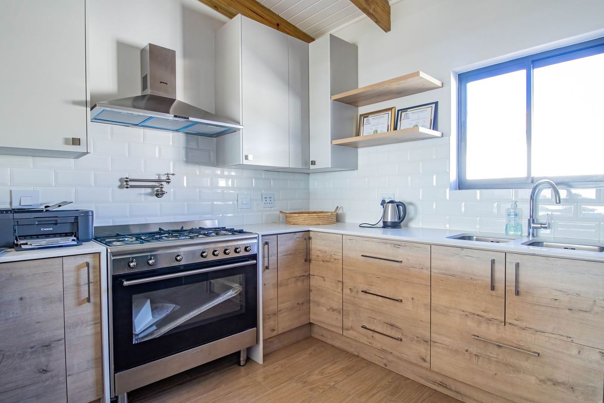 Modern kitchen featuring light wood-grain cabinetry, white subway tile backsplash, stainless steel gas stove with extractor fan, and floating timber shelving.