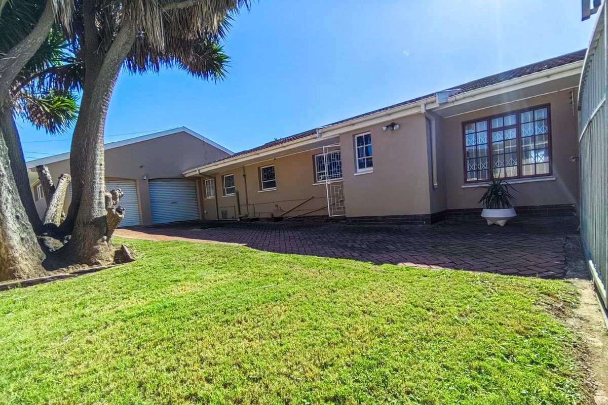 A view of the rear exterior of the house featuring a paved patio area, a well-maintained lawn, and access to the garage.