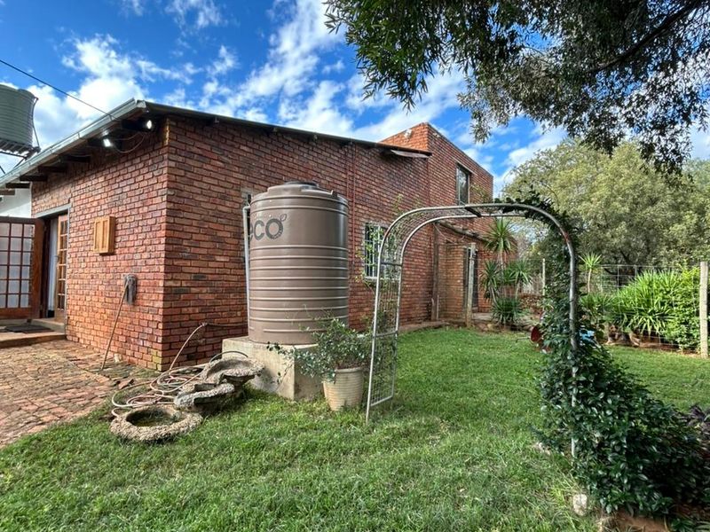 Rear view of a brick farmhouse featuring a water storage tank, garden area, and metal garden archway.