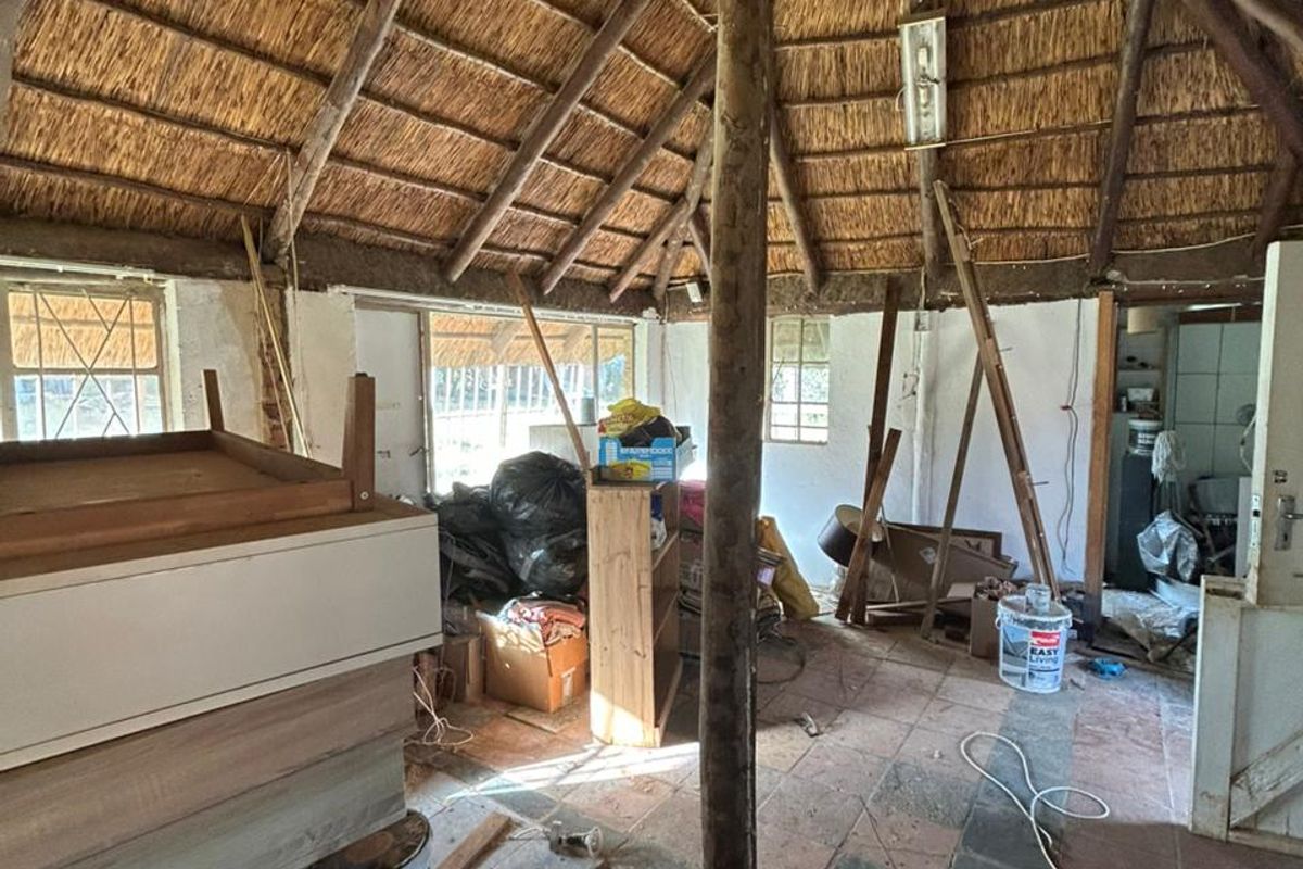 Rustic interior space featuring a traditional thatched roof, exposed timber support beams, and tiled flooring, currently in need of significant renovation and repair.