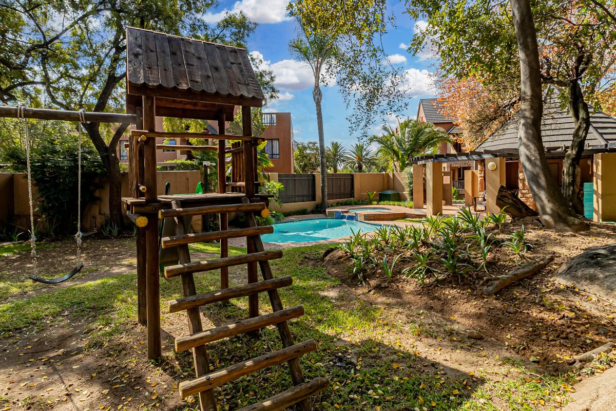 A private backyard featuring a swimming pool, a covered patio area, and a wooden play structure set within a landscaped garden.