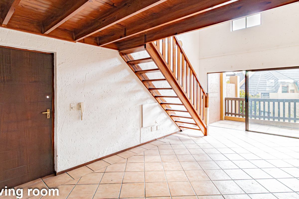 Open-plan living area featuring a wooden staircase, tiled flooring, and sliding glass doors leading to a balcony.