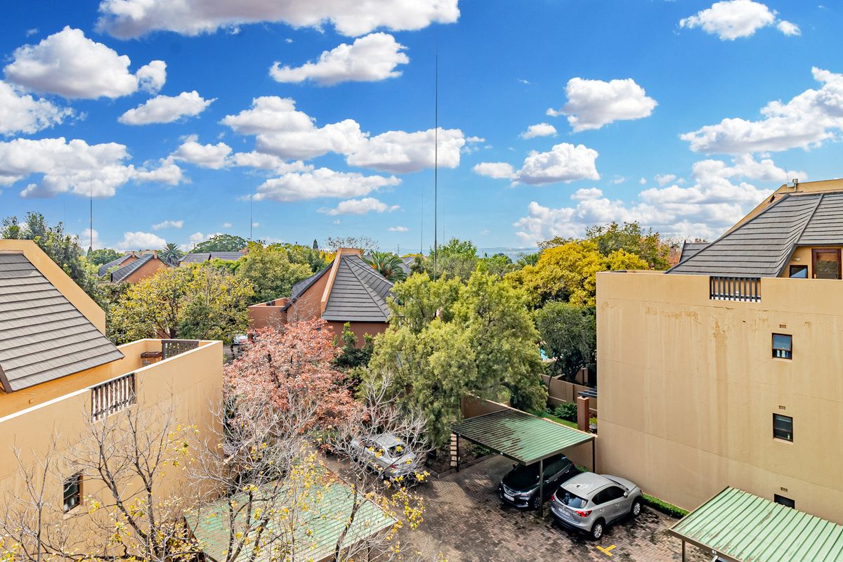 Elevated view of the apartment complex grounds, featuring paved parking areas with covered carports and mature trees within the residential estate.