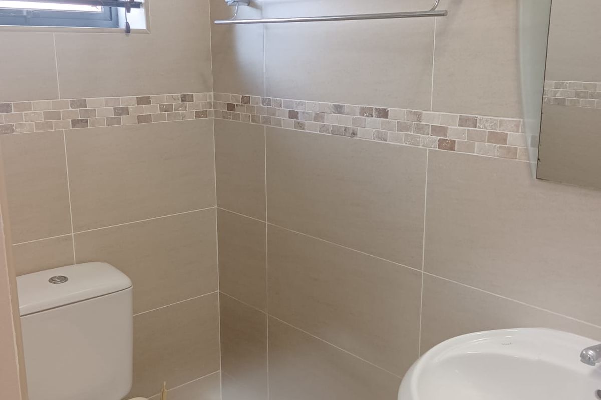 A clean, modern bathroom featuring neutral wall tiles with a decorative mosaic border, a pedestal basin, and a standard toilet.