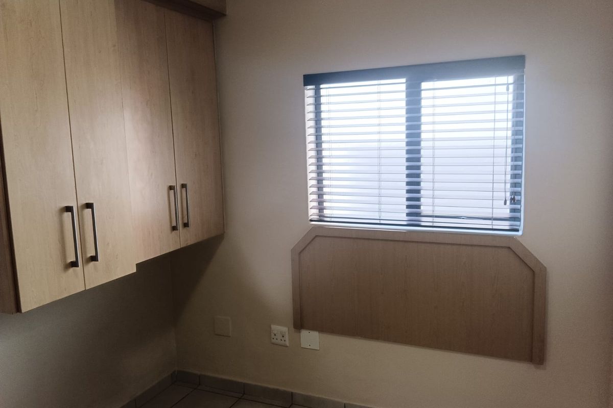 A bedroom featuring built-in wooden cabinetry, a tiled floor, and a window with fitted blinds.