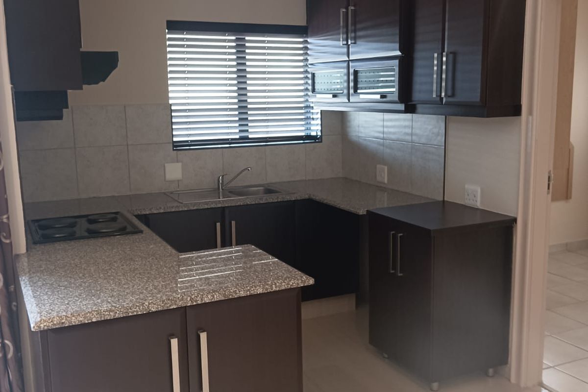 A functional kitchen featuring dark cabinetry, granite countertops, a built-in hob, and tiled flooring, offering a clean and practical workspace.