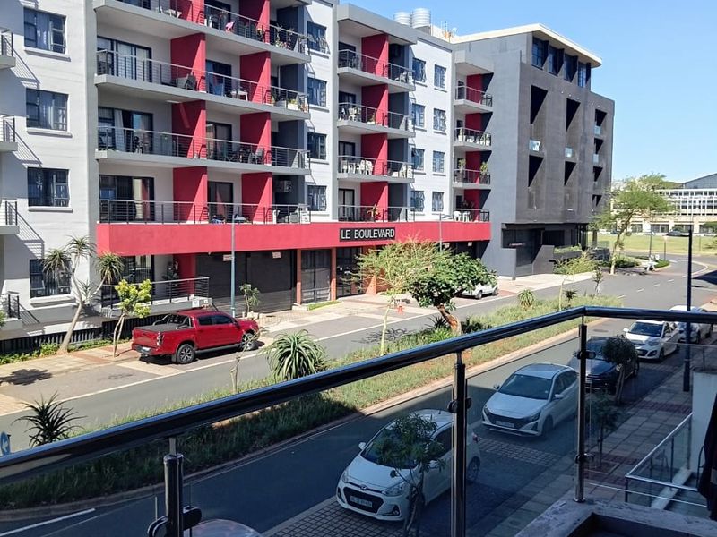 View from a balcony overlooking a modern apartment complex with red accents and street-level parking.