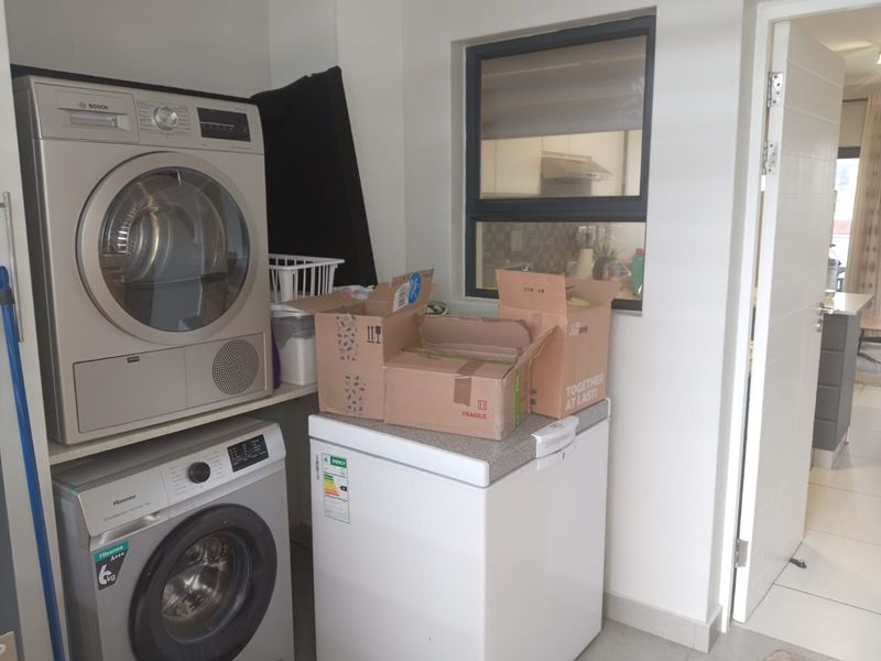 A functional laundry area featuring built-in shelving for appliances and a window providing natural light, with tiled flooring throughout.