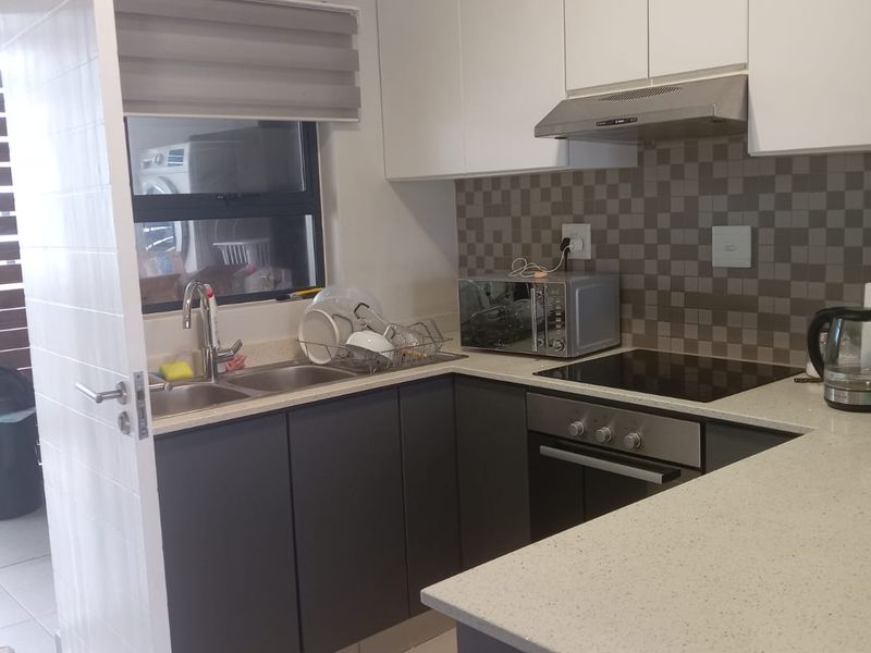 A compact, modern kitchen featuring two-tone cabinetry, stone-look countertops, a built-in oven, hob, and extractor fan with a tiled backsplash.