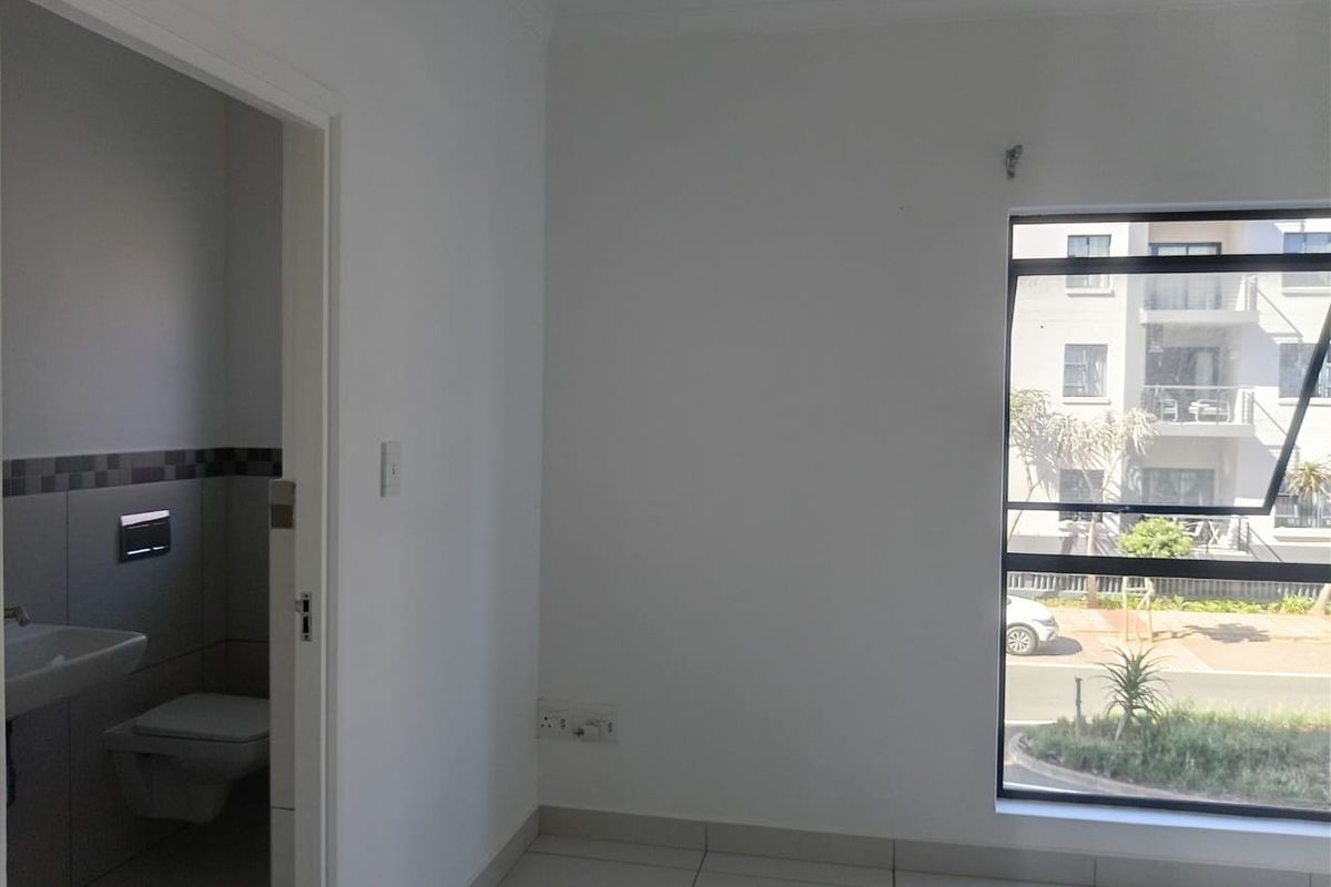 A bright, empty bedroom featuring tiled flooring, a large window, and an adjoining en-suite bathroom with modern fixtures.