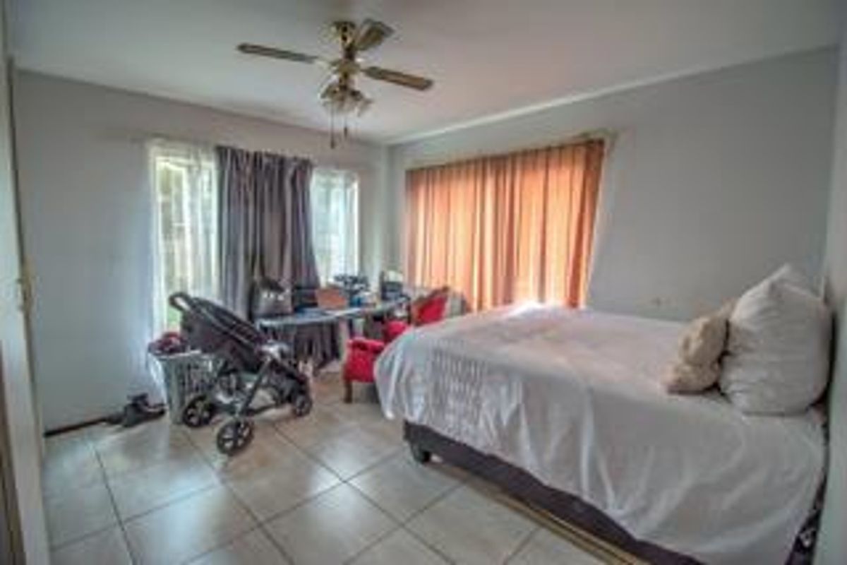 A bedroom featuring tiled flooring and a ceiling fan, with large windows providing natural light.