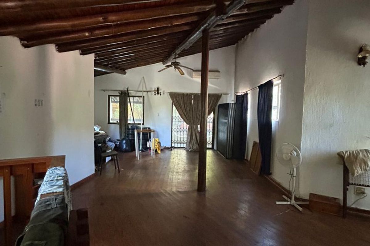 Spacious living area featuring exposed timber beam ceiling, wooden flooring, and direct access to the exterior through a security gate.